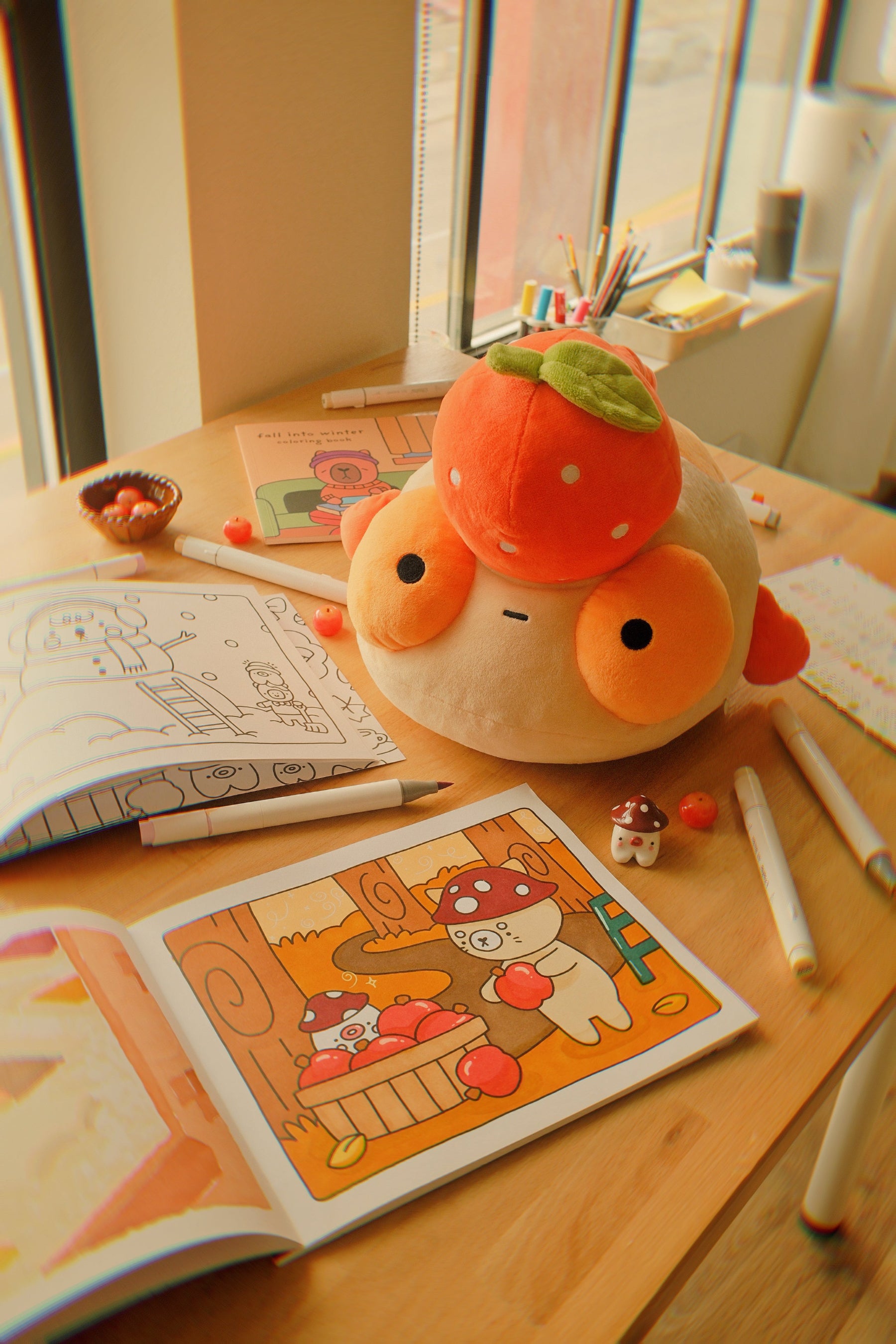 Plush Tangerine Maxine on a table with the Fall into Winter coloring book and art supplies.