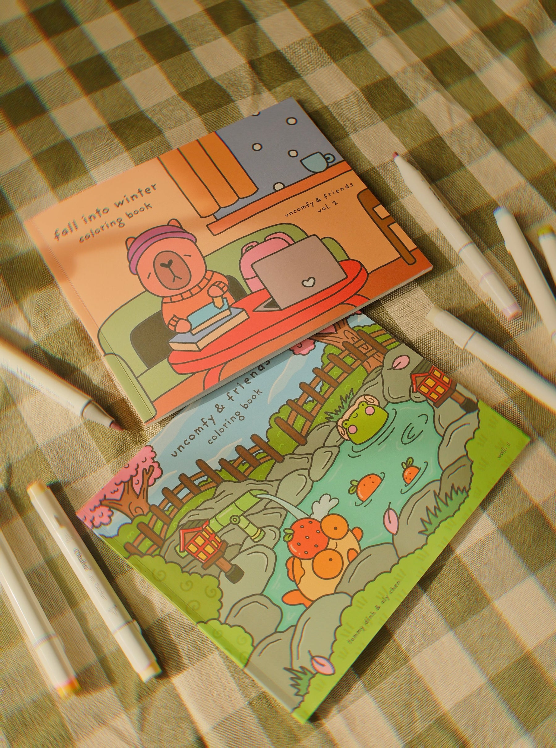 Two coloring books on a checkered surface with markers.