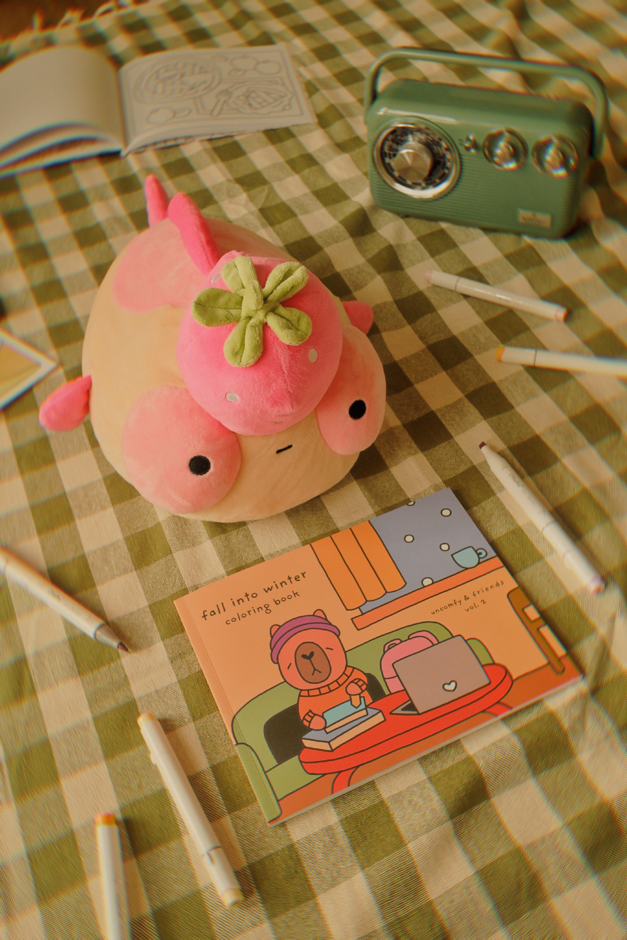 Pink plush Maxine on a checkered tablecloth with a coloring book and pens