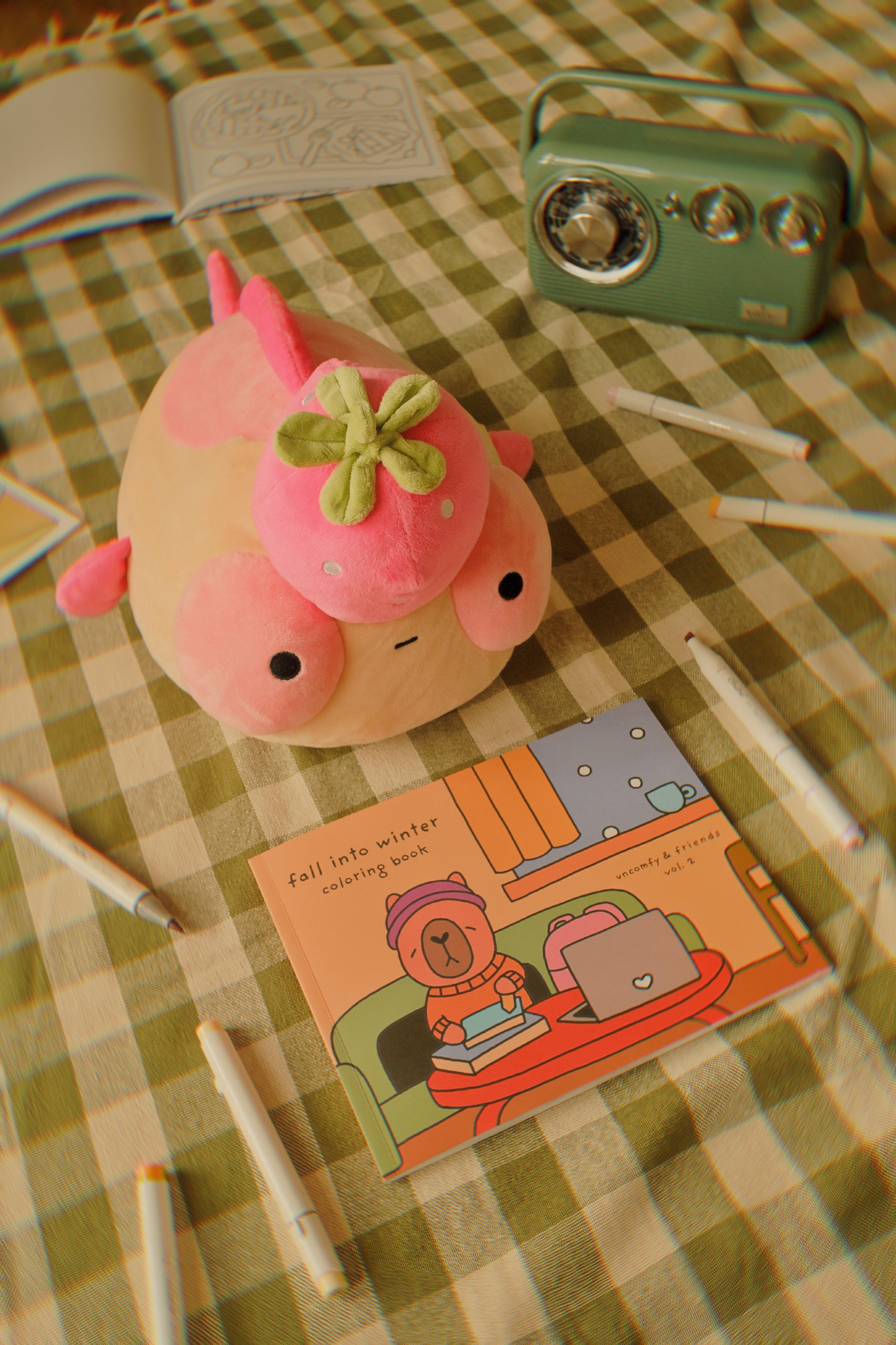Pink plush Maxine on a checkered tablecloth with a coloring book and pens