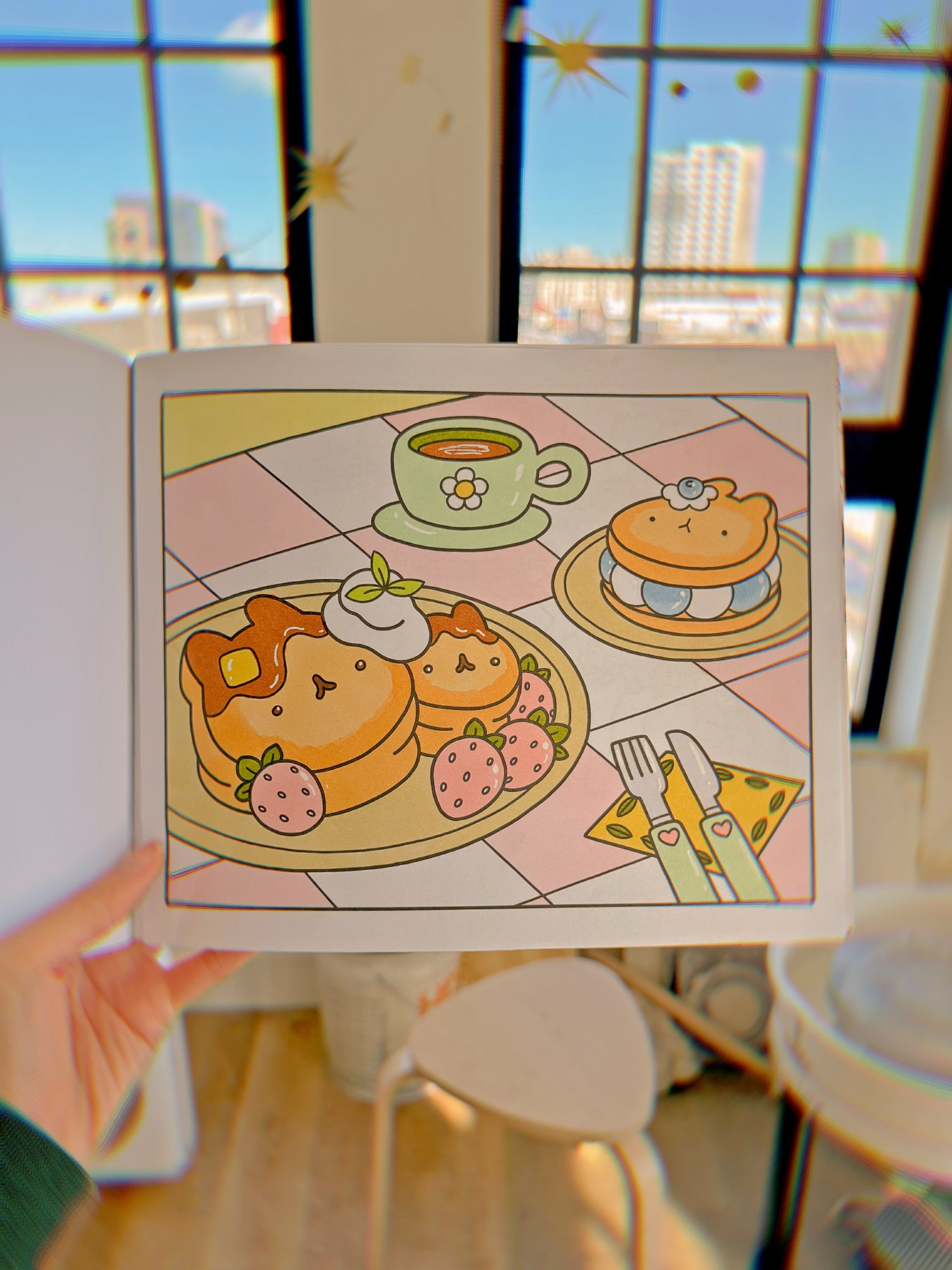Uncomfy holding open a colored in page of the coloring book in front of her apartment. In the background you can see her pottery wheel and the Denver skyline through the windows. 